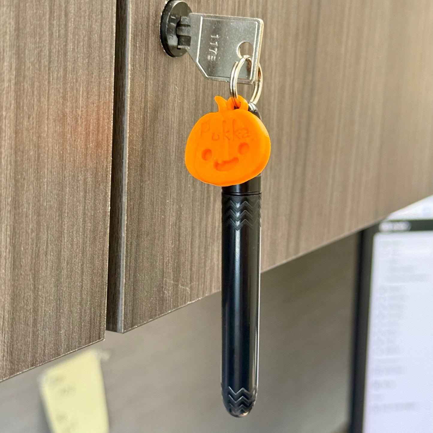 Black pen with orange keychain attached to a wooden surface