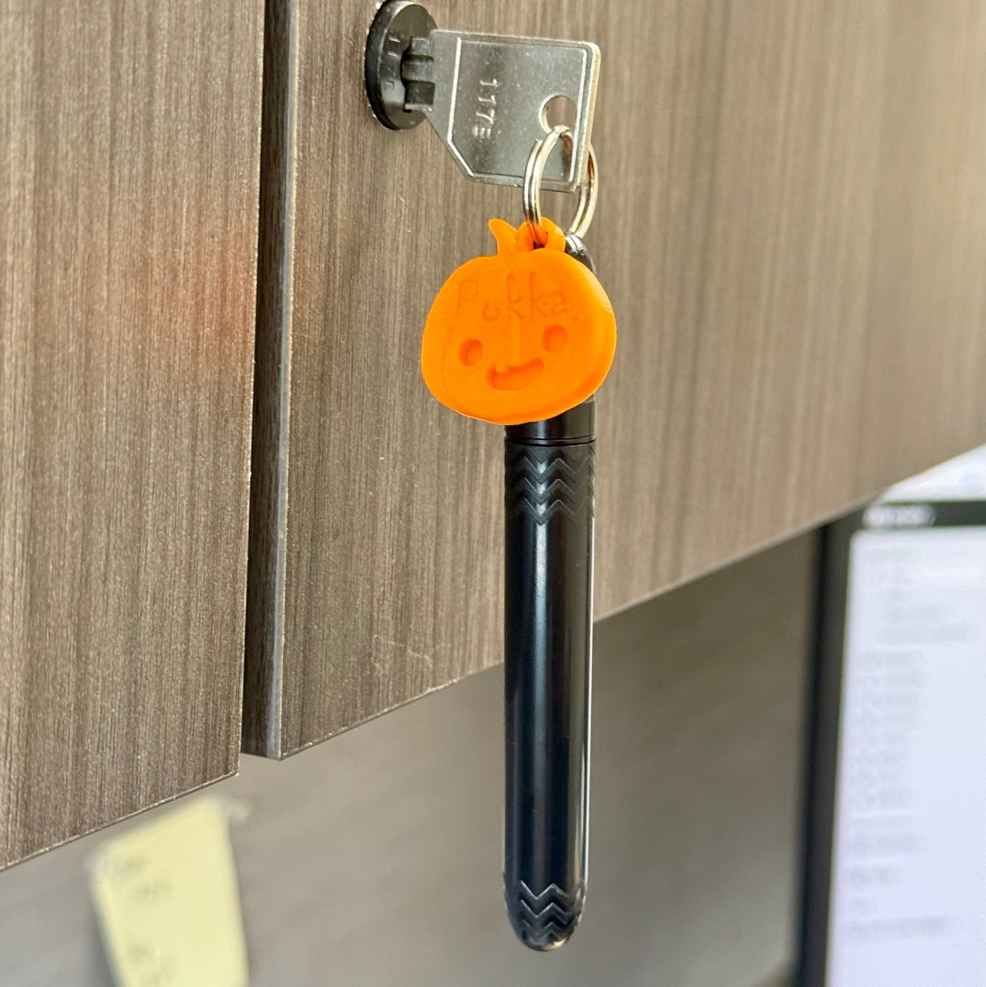 Black pen with orange keychain attached to a wooden surface