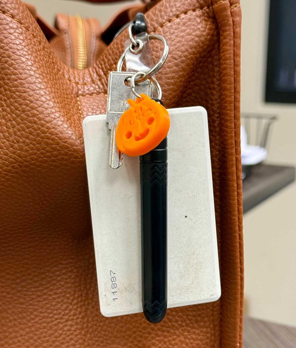 Black vape pen with orange cap and keychain on a white card against a brown leather background