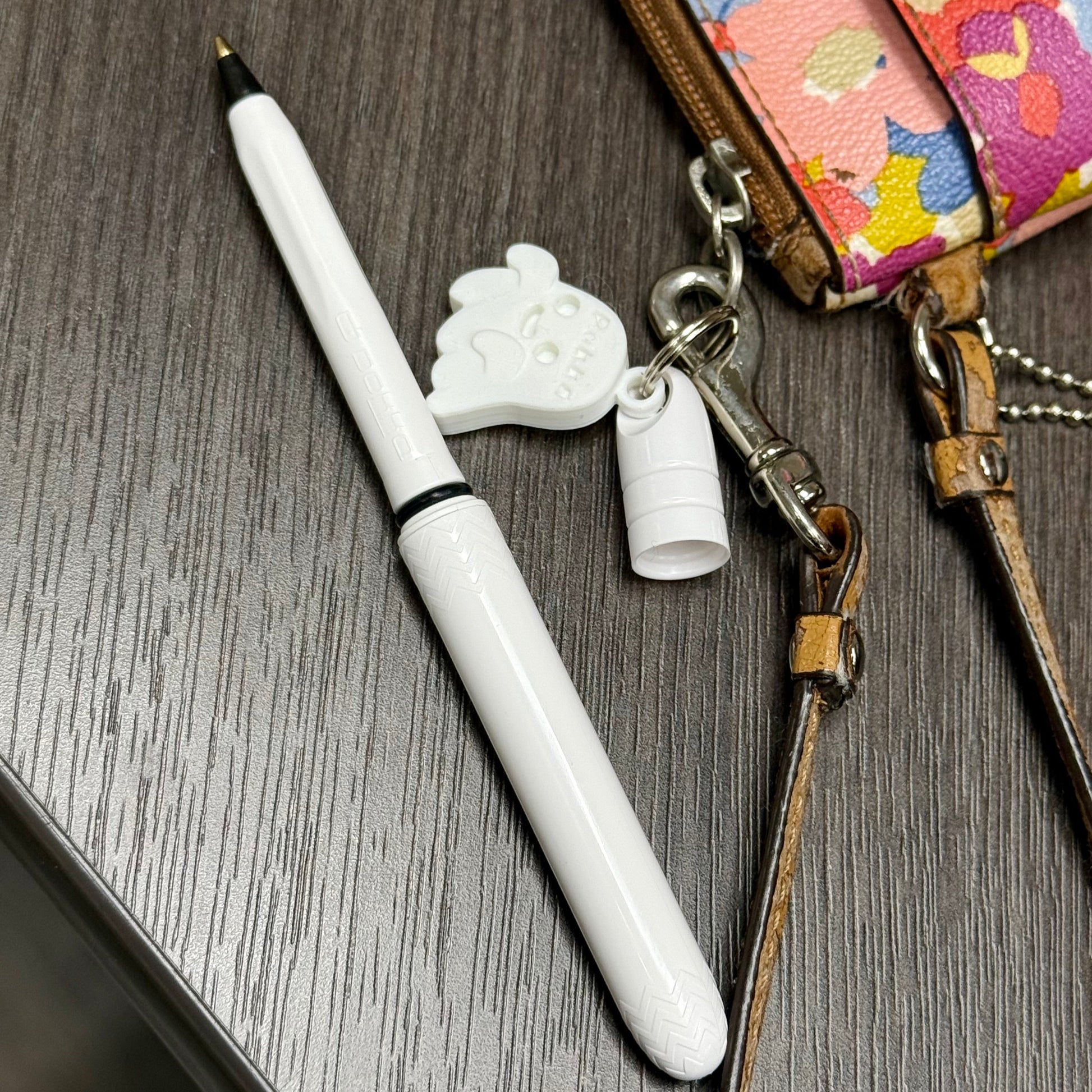 White pen with a decorative cap on a wooden surface next to a colorful wallet.