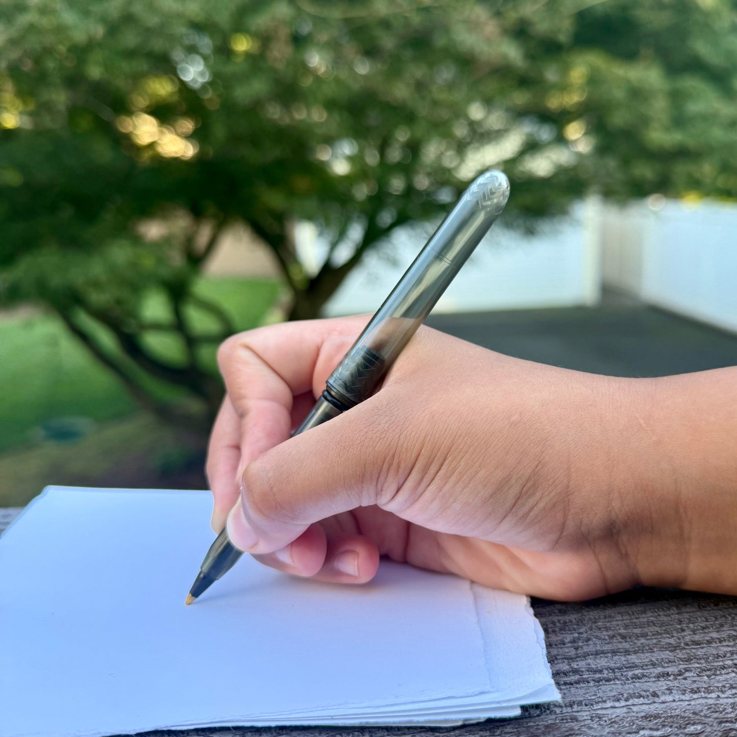 Hand writing on a piece of paper with a pen, outdoors.
