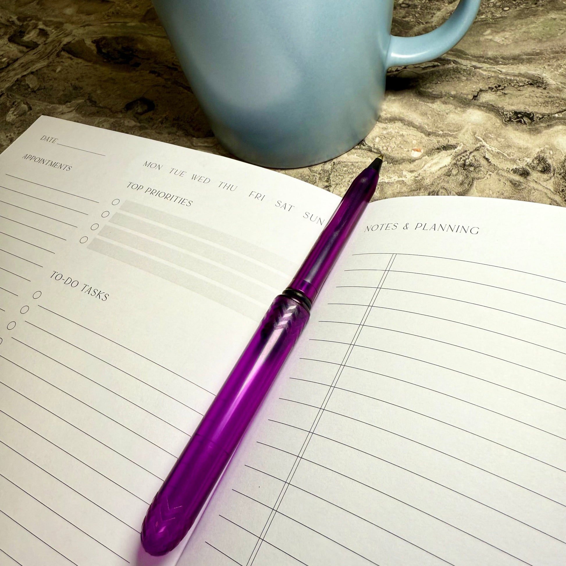 Purple pen on a planner with a blue mug in the background