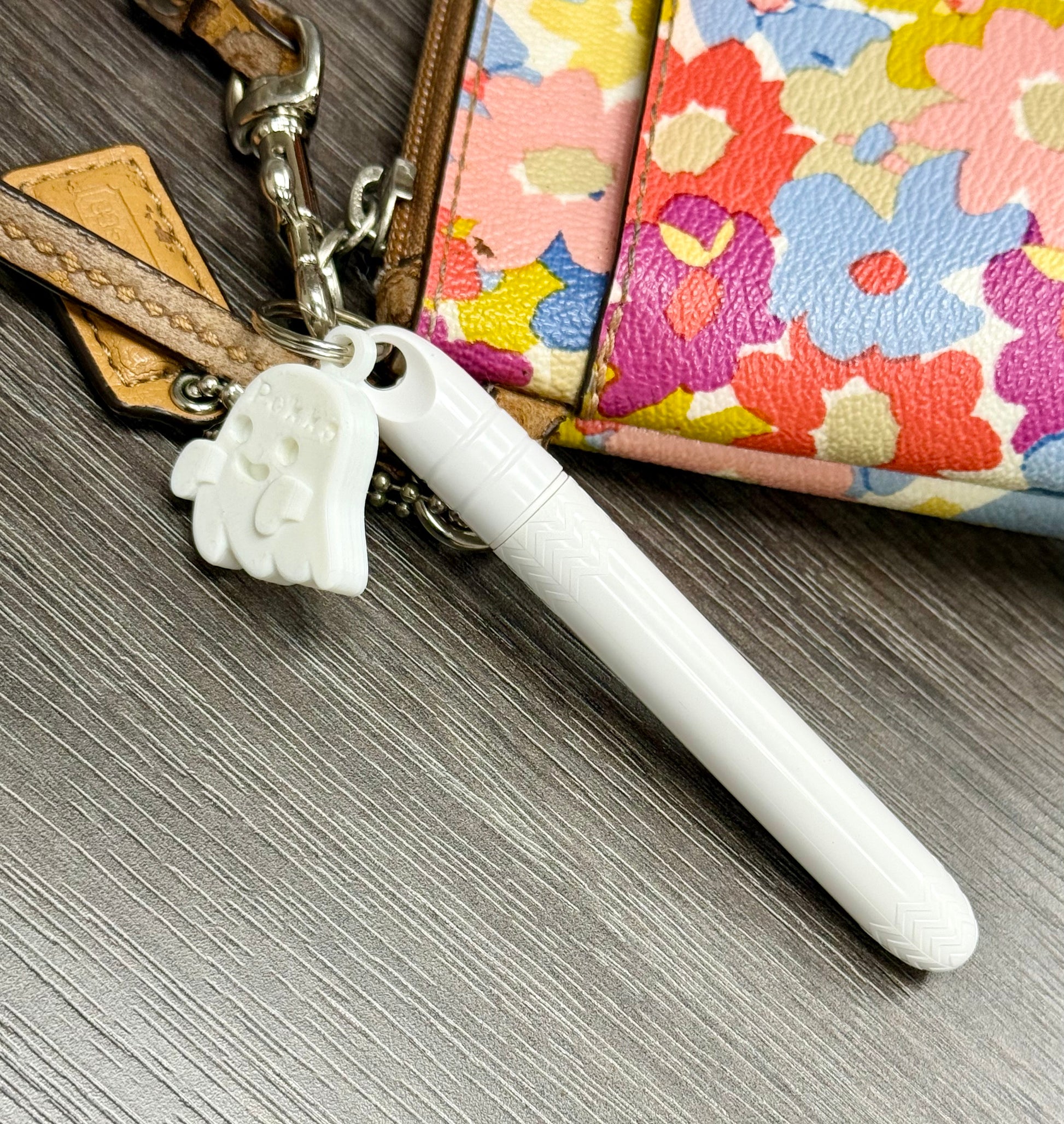 White keychain with paw design attached to a colorful floral purse on a wooden surface