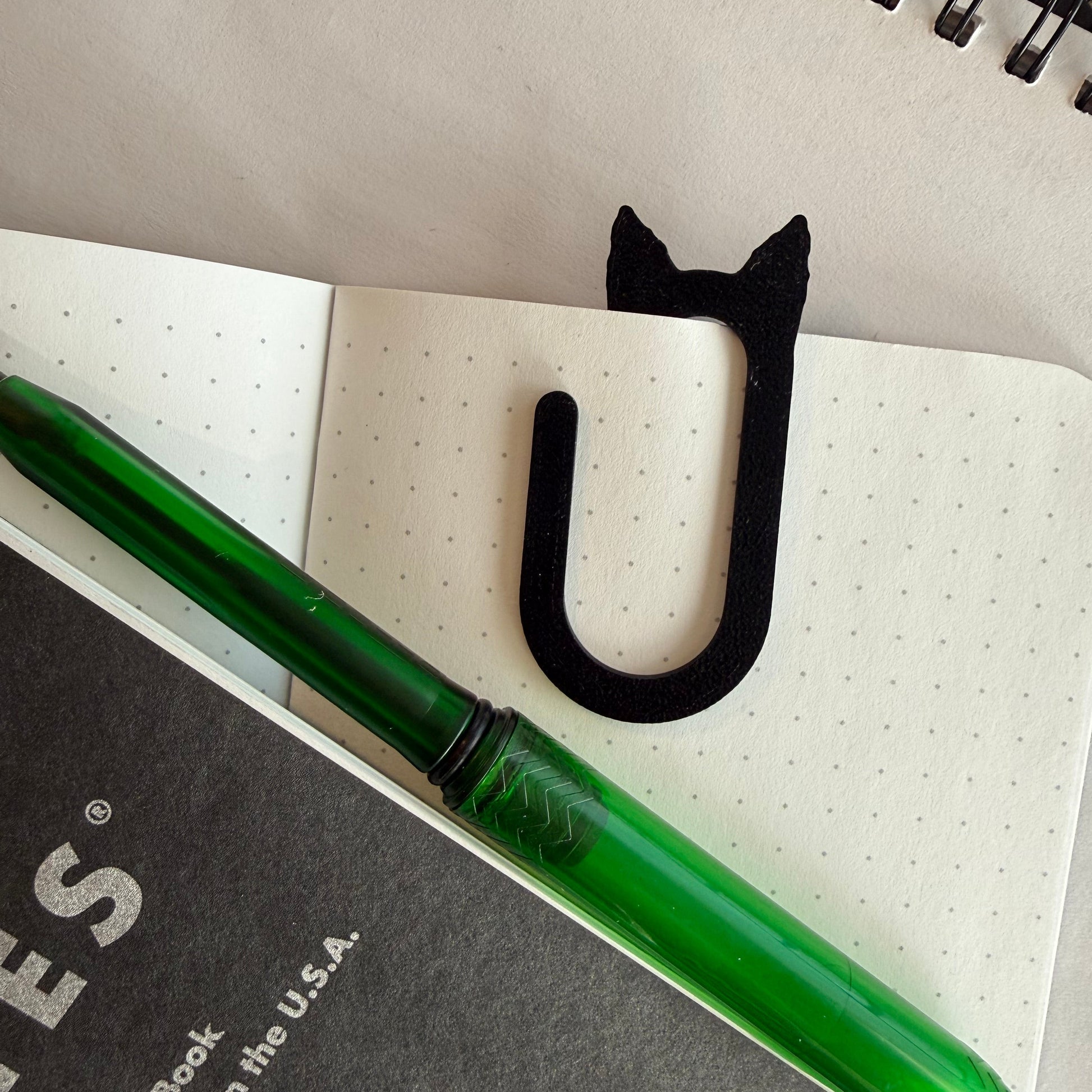 Green pen on a notebook with a black cat-shaped object