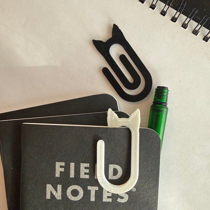 Field Notes notebook with a white keychain on top, surrounded by other small items on a light surface.