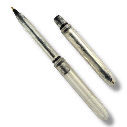 A transparent ballpoint pen with its cap removed, showing the black ink tip and the medium ballpoint nozzle.