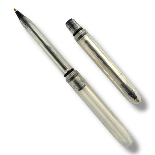 A transparent ballpoint pen with its cap removed, showing the black ink tip and the medium ballpoint nozzle.