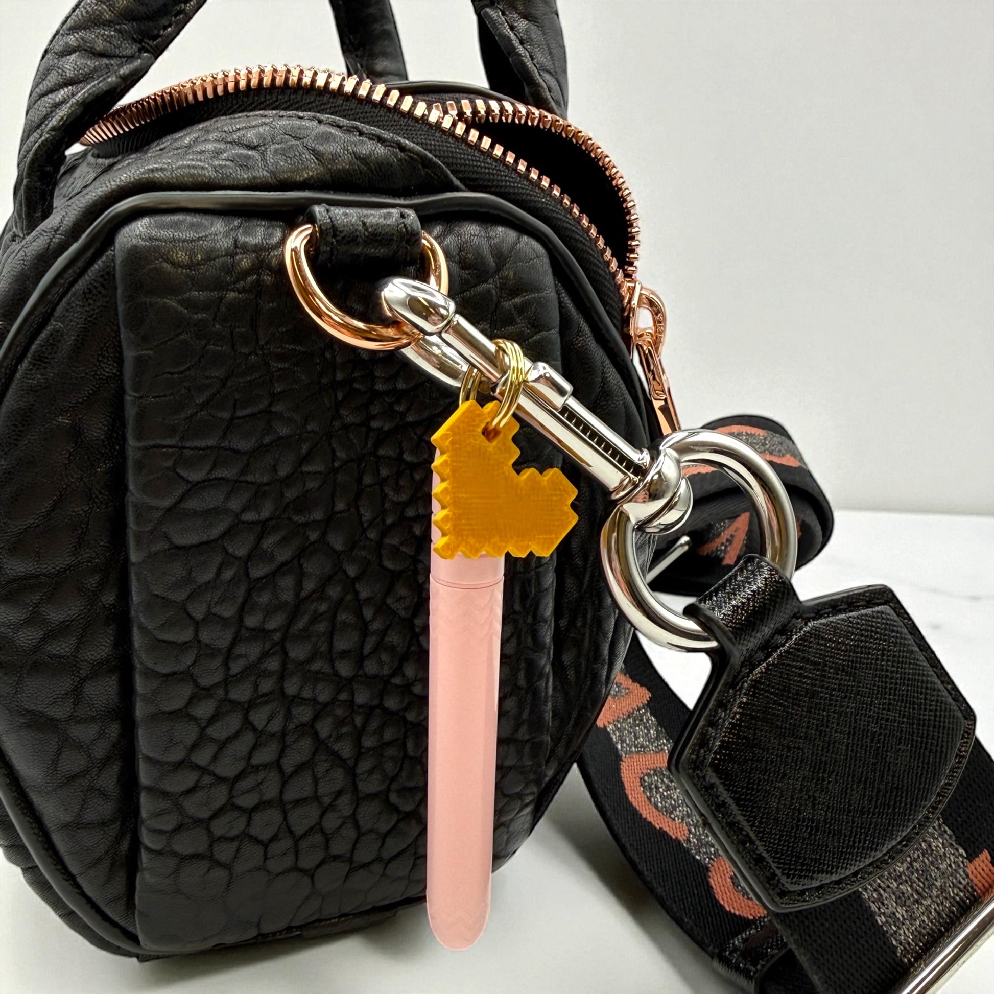Black textured handbag with a keychain featuring a pink object and yellow heart-shaped tag.