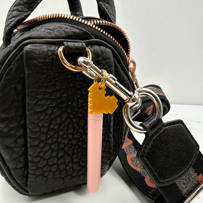 Black textured handbag with a keychain featuring a pink object and yellow heart-shaped tag.