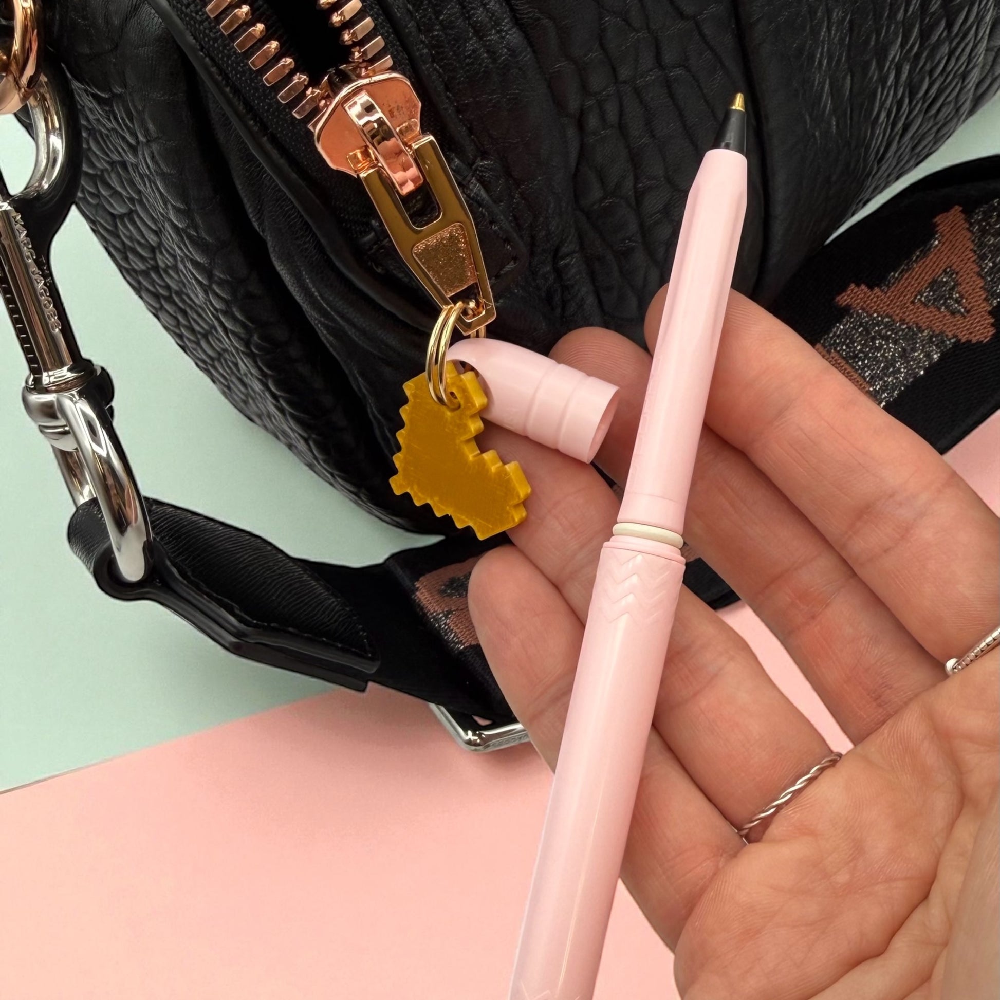 Person holding a pink pen with a black textured bag in the background