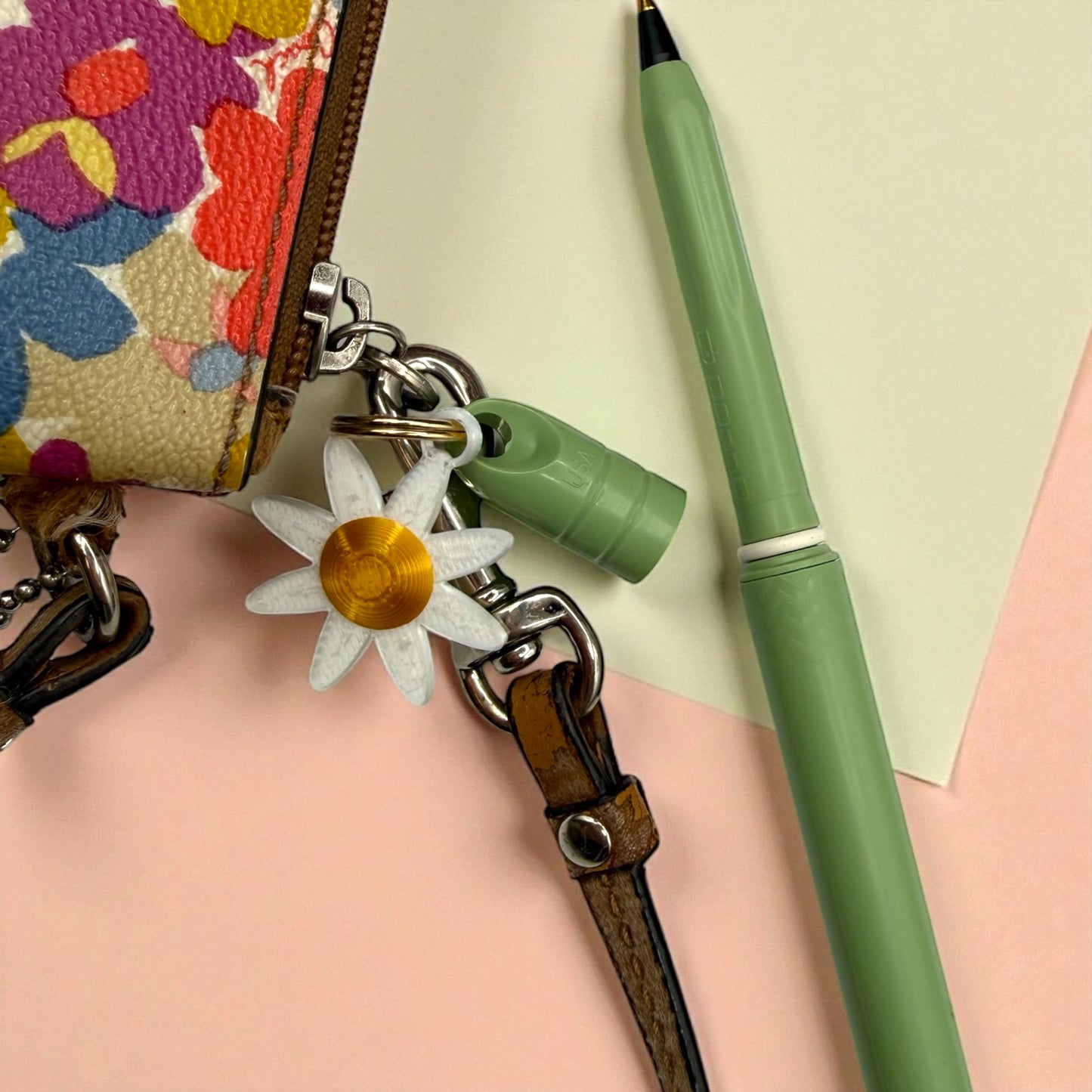 Green pen with floral charm on a pink surface