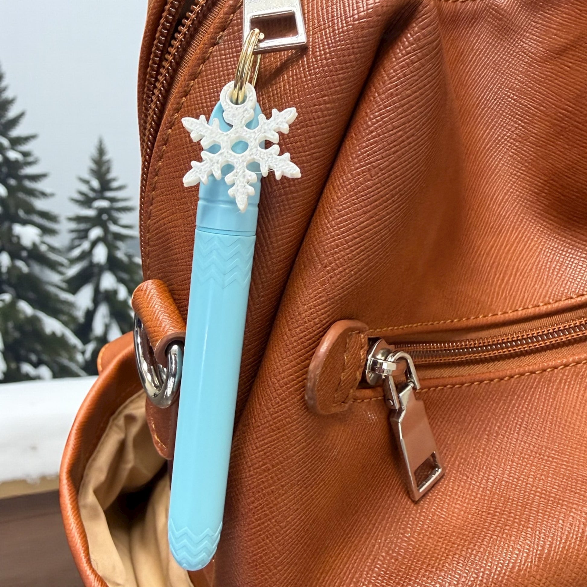 Blue pen with snowflake charm attached to a brown leather bag outdoors.