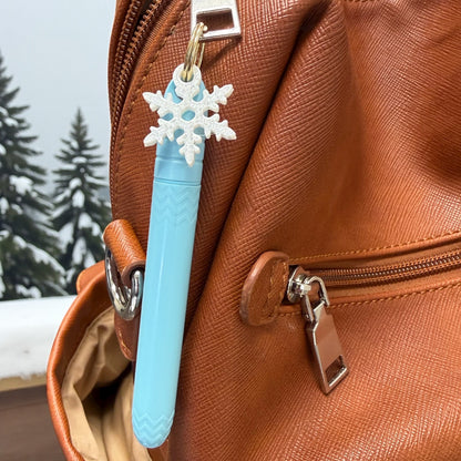 Blue pen with snowflake charm attached to a brown leather bag outdoors.