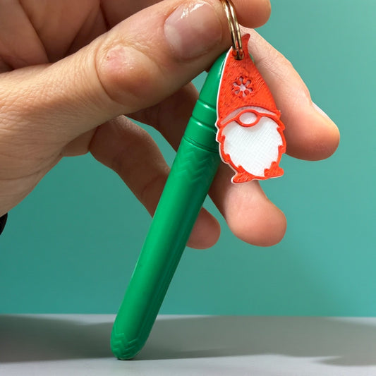 Green pen with a red and white gnome-shaped keychain held by a hand against a teal background