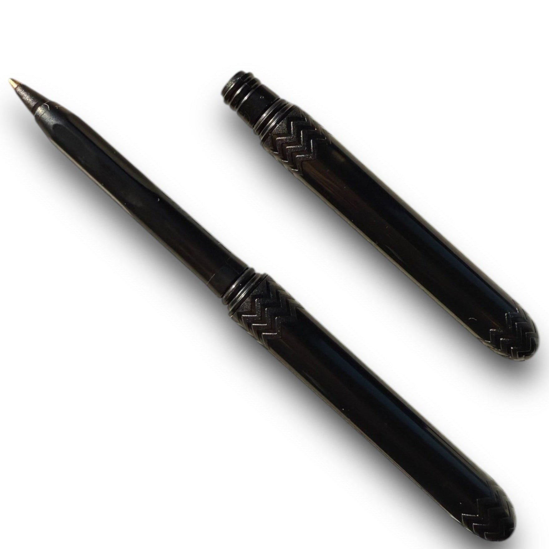 A black ballpoint pen with its cap removed, displaying the tip and the black ink. The pen is designed with a pattern near the base.