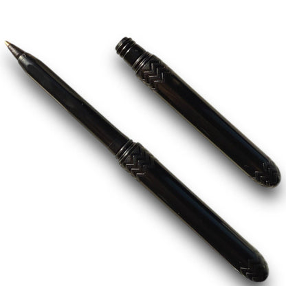 A black ballpoint pen with its cap removed, displaying the tip and the black ink. The pen is designed with a pattern near the base.